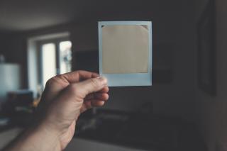 Hand holding up an Polaroid picture that hasn't developed yet inside a house.